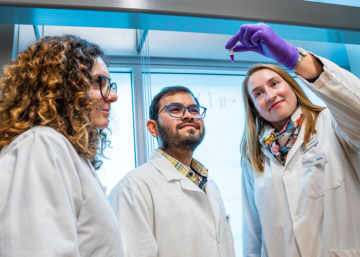 Three researchers in a lab taking a look at liquid.